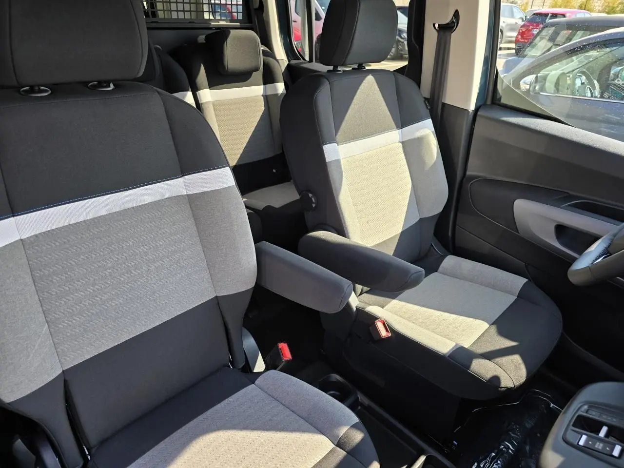 Vue intérieure rapprochée des sièges avant gris et noirs du Citroën Berlingo 2025 avec accoudoir central côté droit.