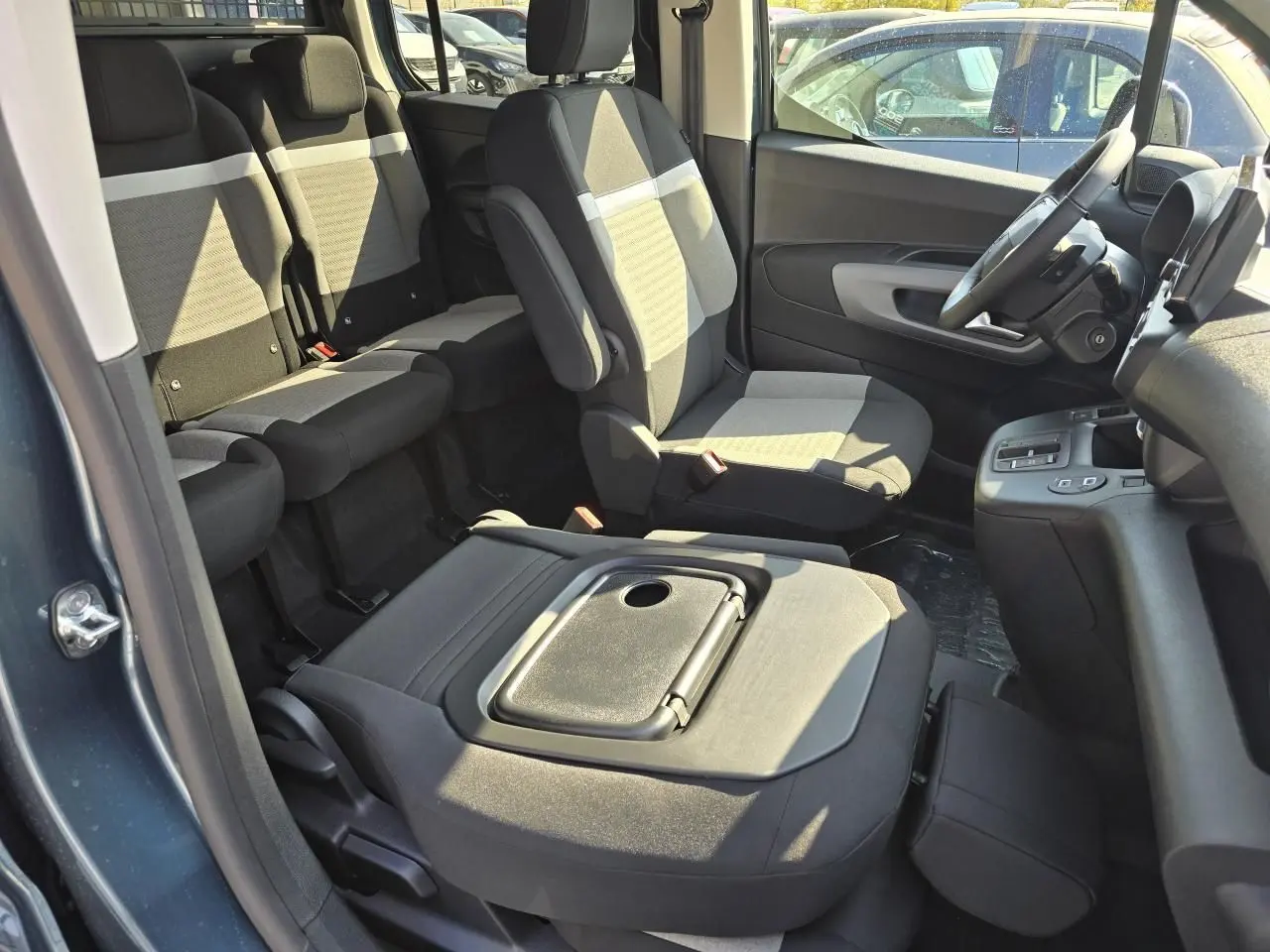 Intérieur du Citroën Berlingo 2025 bleu Kiama, vue côté droit sur sièges tissu gris avec tablette aviation rabattue.