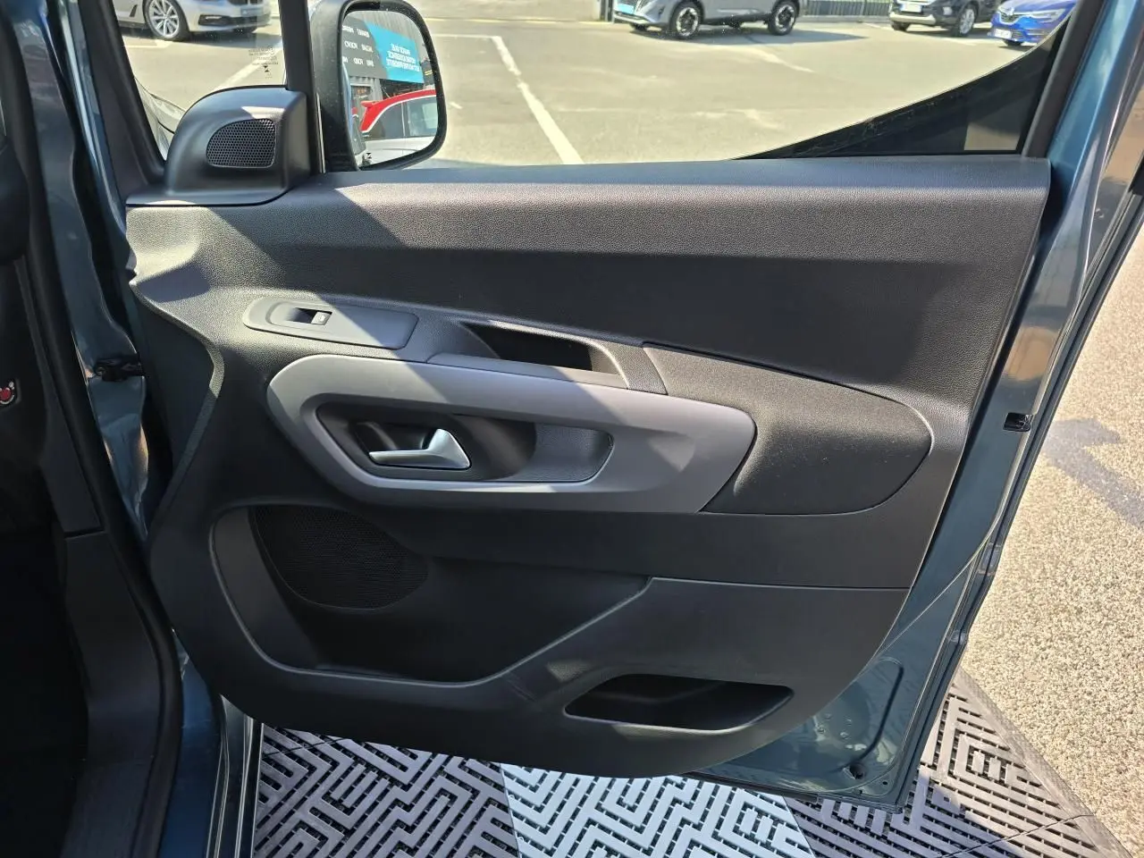 Vue côté gauche de la porte avant ouverte d'un Citroën Berlingo bleu Kiama métal, avec commandes électriques et haut-parleur intégré.