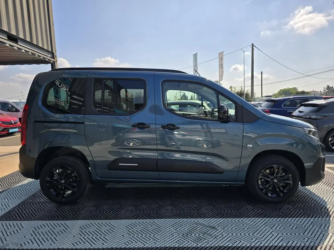 Profil latéral droit du Citroën Berlingo bleu Kiama métallisé avec vitres arrière teintées et jantes noires.