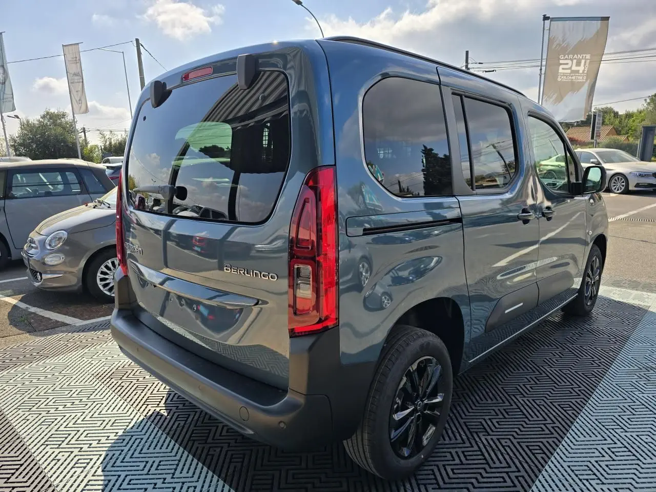 Vue 3/4 arrière droite du Citroën Berlingo bleu Kiama métallisé avec vitres arrière teintées et jantes noires.