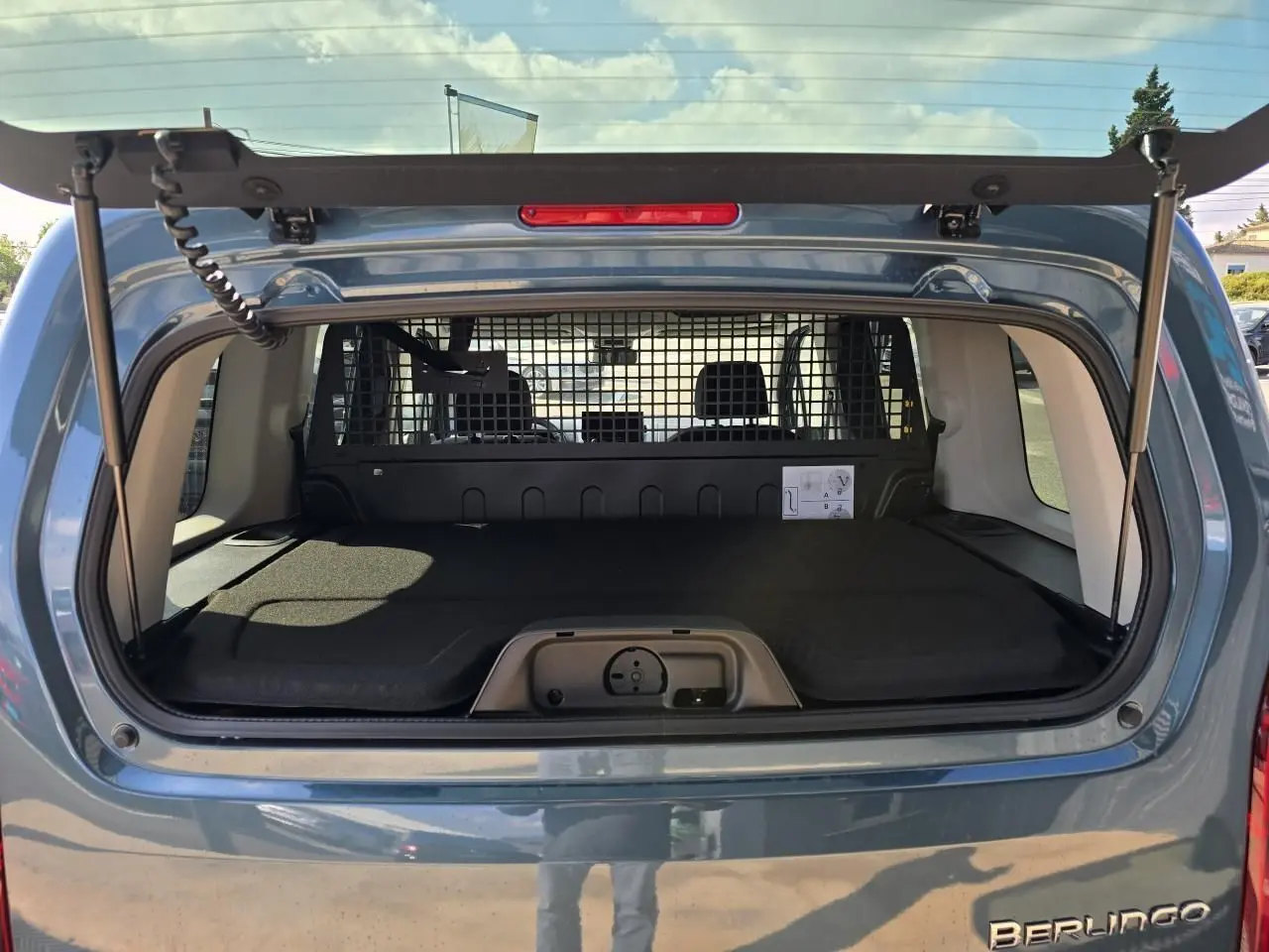Vue arrière du coffre ouvert d'un Citroën Berlingo bleu Kiama Métal avec séparation grillagée et plancher plat.