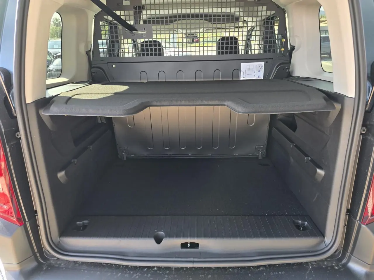 Coffre ouvert vu de l'arrière du Citroën Berlingo III Bleu Kiama Métal avec séparation grillagée et tablette de rangement.