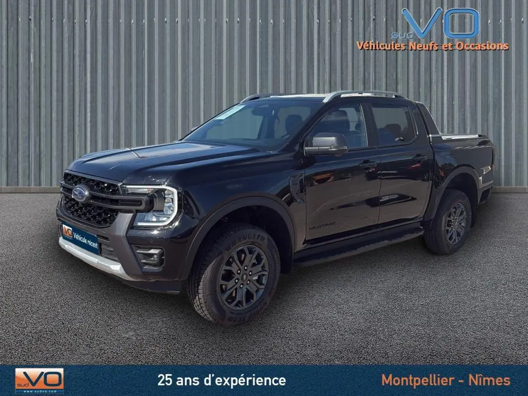 Ford Ranger Wildtrak noir en 3/4 avant droit, avec barres de toit, marchepieds et jantes alliage 18 pouces visibles.