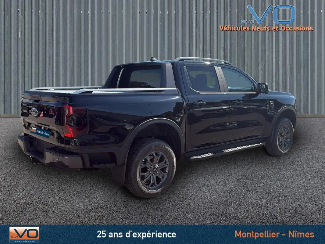 Ford Ranger Wildtrak noir en 3/4 arrière droit, avec barres de toit, marchepieds et jantes alliage 18 pouces.