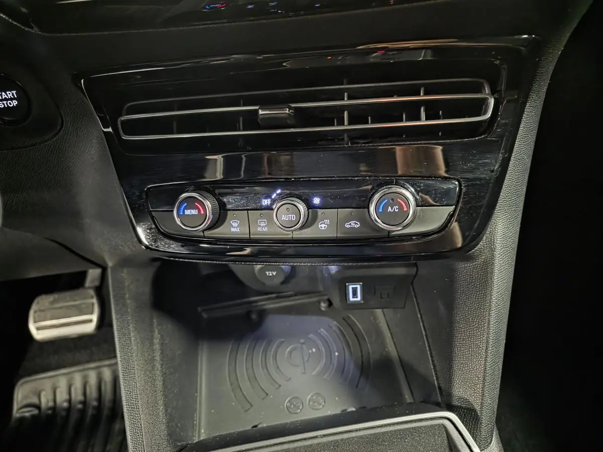 Vue rapprochée de la console centrale noire de l’Opel Mokka-e 2025, avec commandes climatisation et recharge smartphone par induction.
