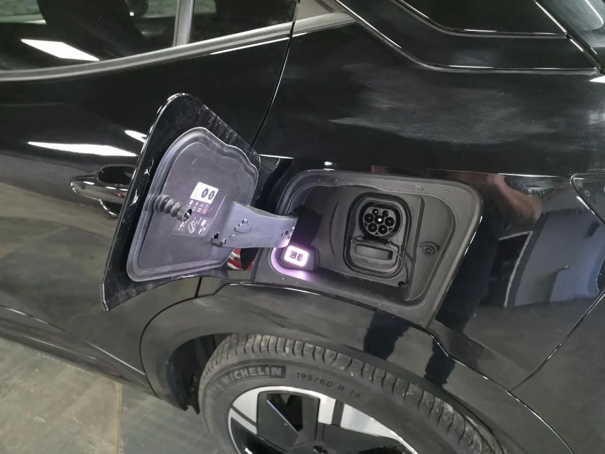 Vue côté gauche arrière d'un Opel Mokka-e noir avec trappe de recharge électrique ouverte et prise visible.