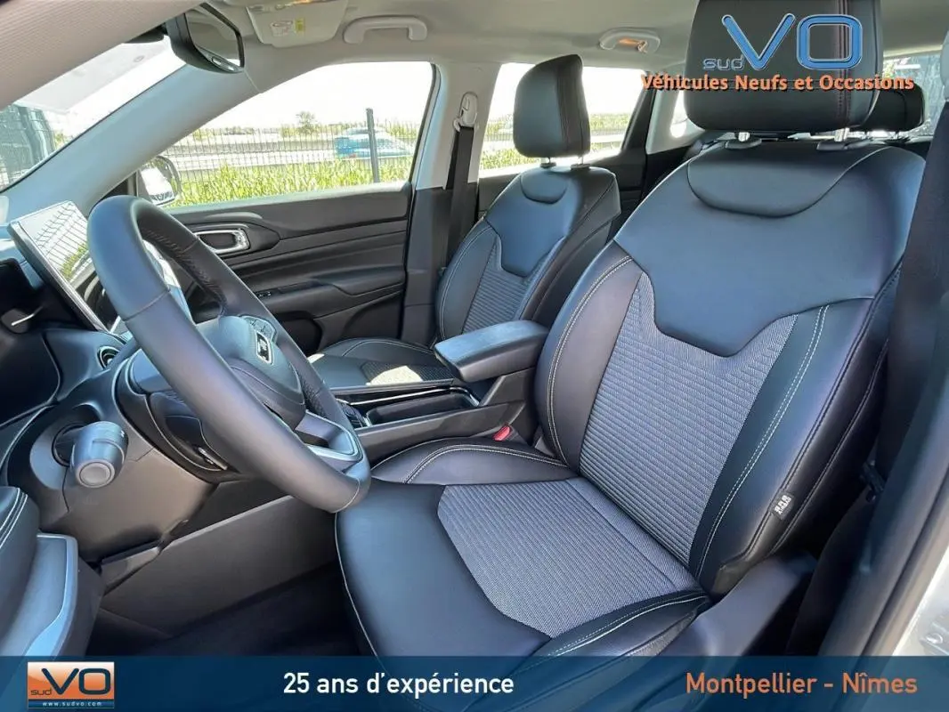 Vue intérieure côté conducteur du Jeep Compass blanc 2024, sièges en cuir noir avec accoudoir central et volant multifonction.
