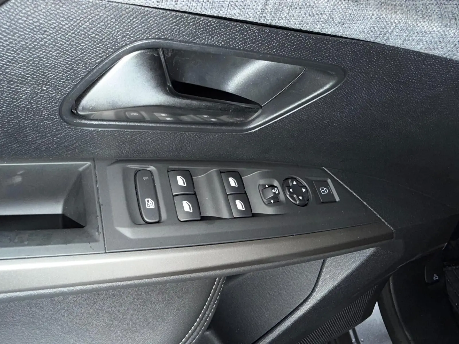 Gros plan sur la commande des vitres électriques et la poignée intérieure côté gauche du Peugeot 3008 gris 1.2 HYBRID 136 ALLURE.