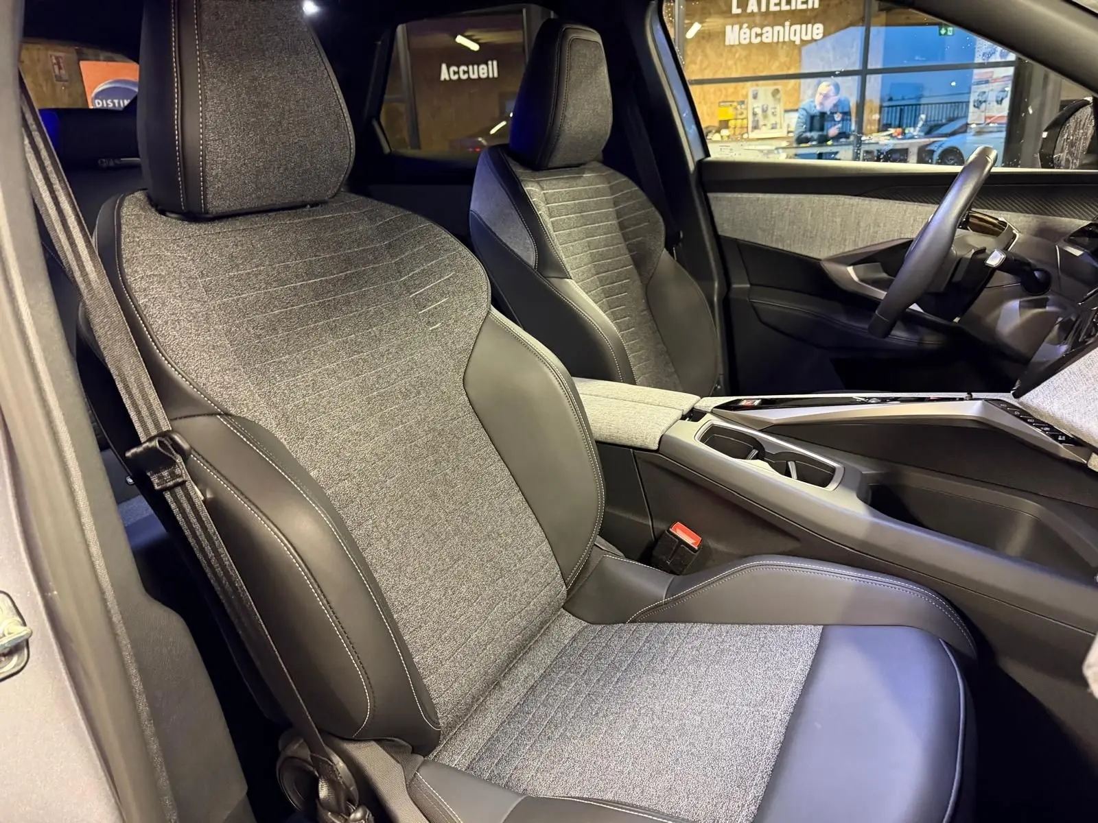 Vue intérieure côté droit du Peugeot 3008 1.2 HYBRID 136 Allure 2025, sièges tissu gris et cuir noir, console centrale visible.