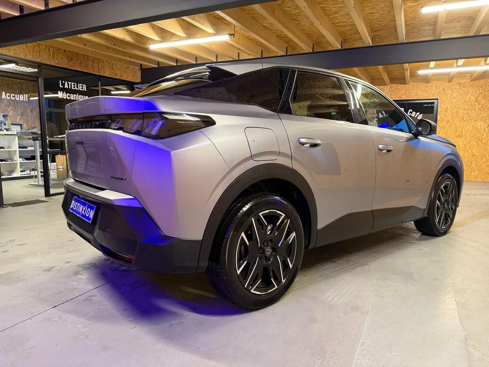 Vue 3/4 arrière droite du Peugeot 3008 gris hybride 2025, avec jantes noires et toit noir contrasté en intérieur d'atelier.
