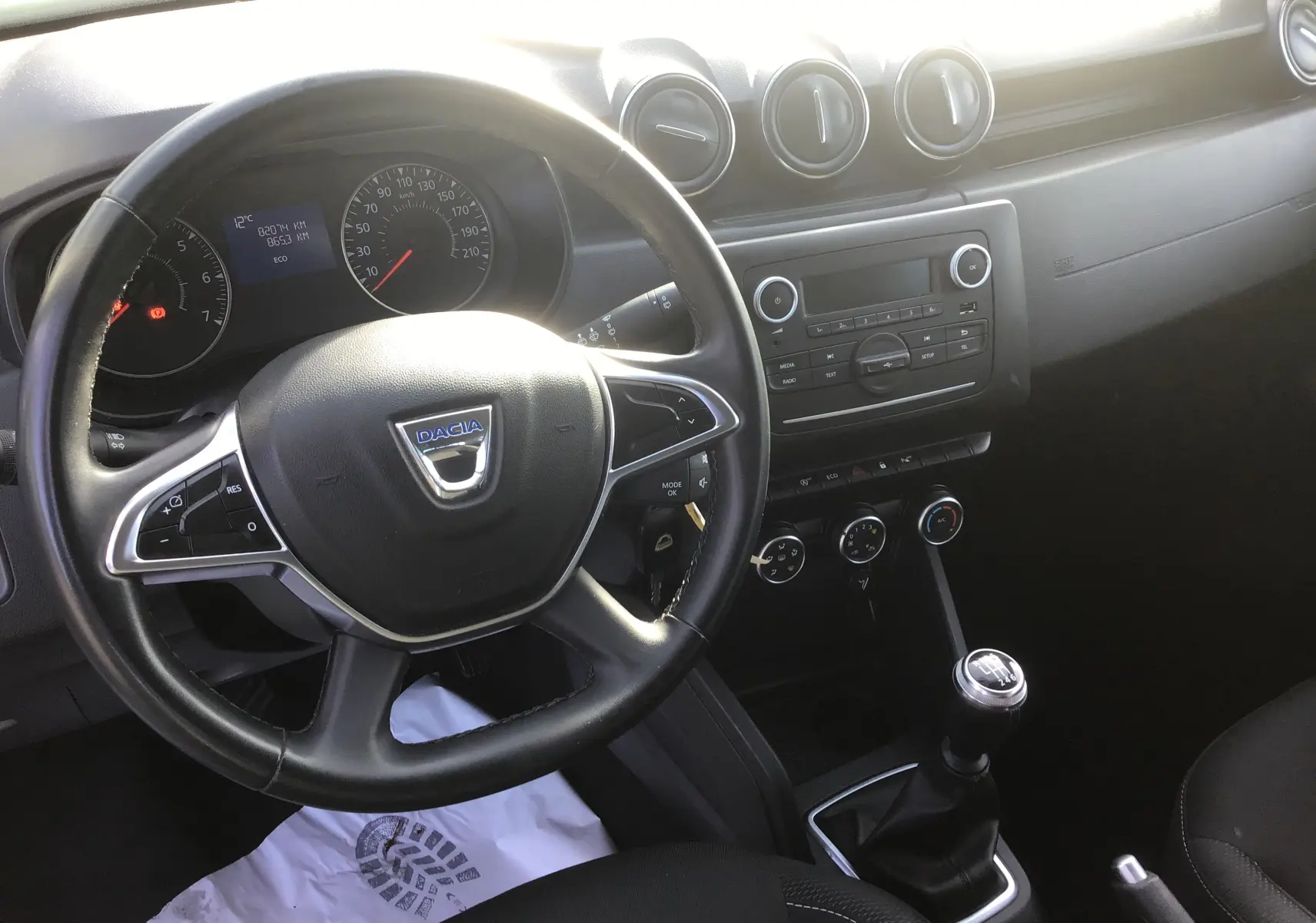 Vue intérieure du tableau de bord et volant noir du Dacia Duster 2021 avec levier de vitesse manuel et commandes centrales visibles.