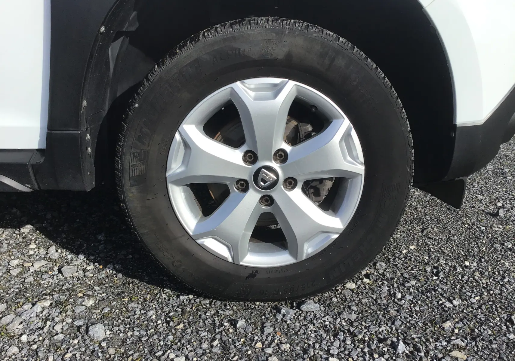 Gros plan sur la roue avant droite du Dacia Duster blanc 2021 avec jante alliage 16 pouces et logo central Dacia.