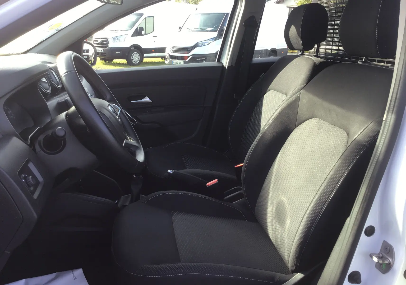 Vue intérieure côté conducteur du Dacia Duster blanc 2021, sièges noirs avec grille de séparation visible derrière.