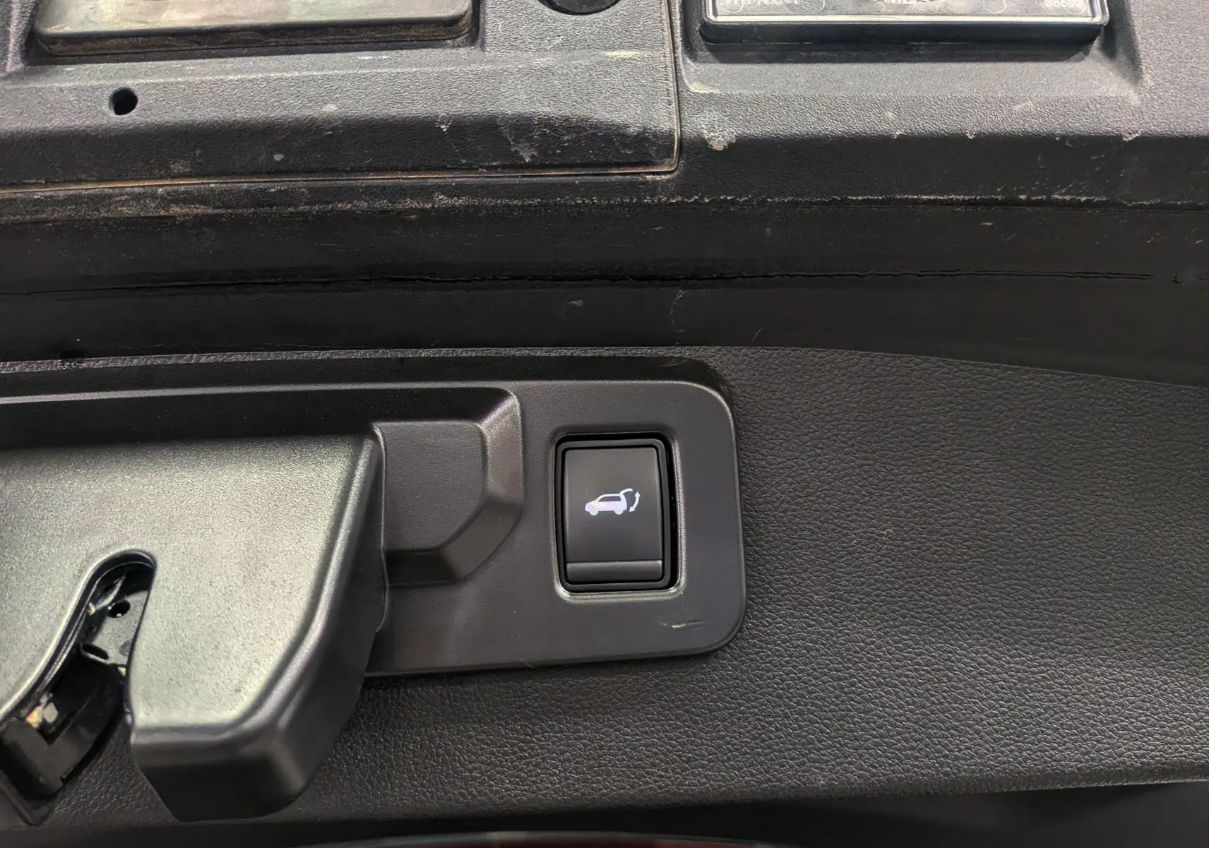 Bouton d'ouverture électrique du coffre sur panneau intérieur noir d'un Renault SYMBIOZ E-TECH gris Cassiopé.