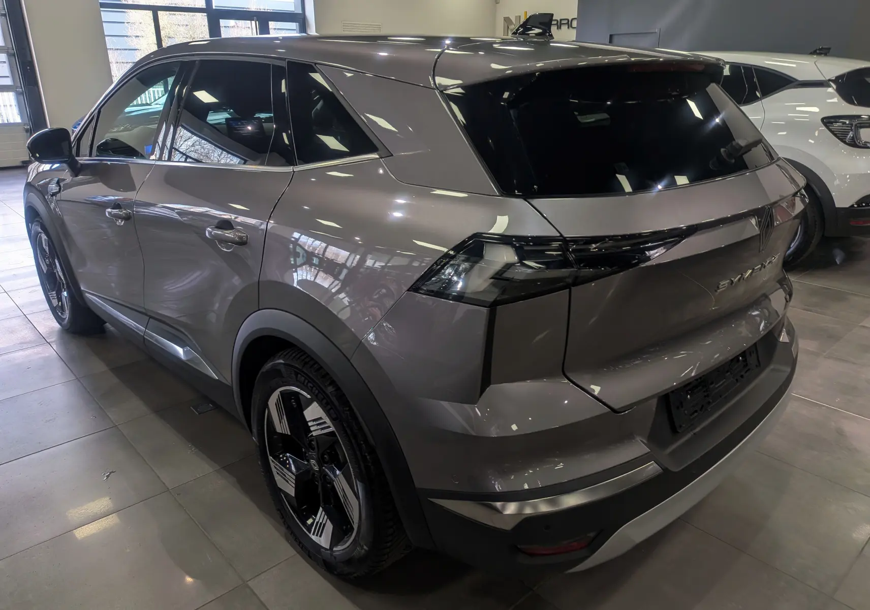 Vue 3/4 arrière droite du Renault SYMBIOZ gris Cassiopé avec feux arrière LED et jantes bicolores en concession.