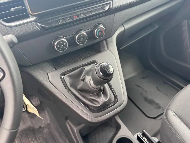 Vue intérieure rapprochée côté conducteur du levier de vitesses manuel et des commandes de climatisation du Renault Kangoo blanc 2024.