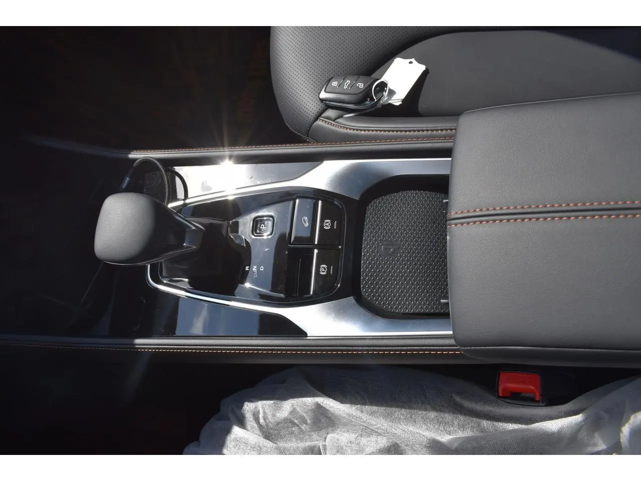 Vue plongeante sur la console centrale noire du MG Motor EHS 1.5 Hybrid+ avec levier de vitesses et clé posée sur accoudoir cuir.