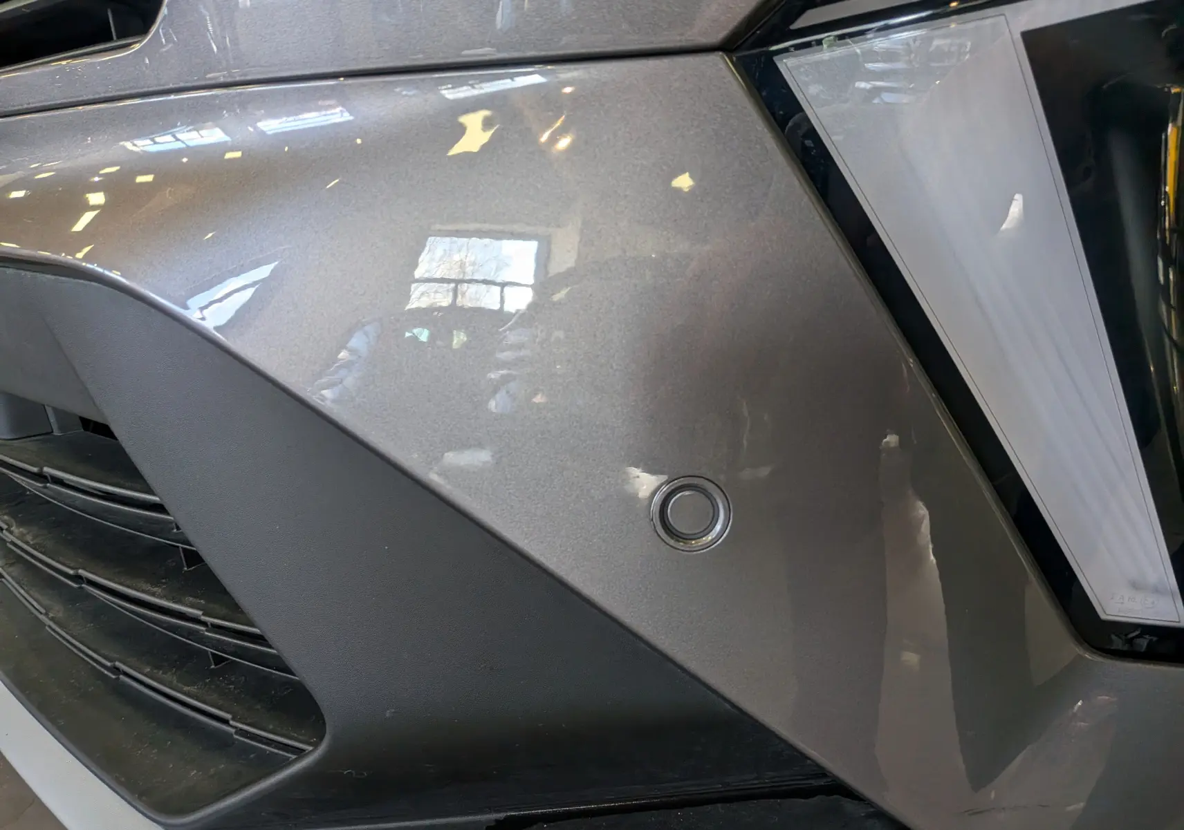 Gros plan sur l’avant droit gris Cassiopé du Renault Symbioz E-TECH, avec capteur de stationnement et partie de calandre noire.