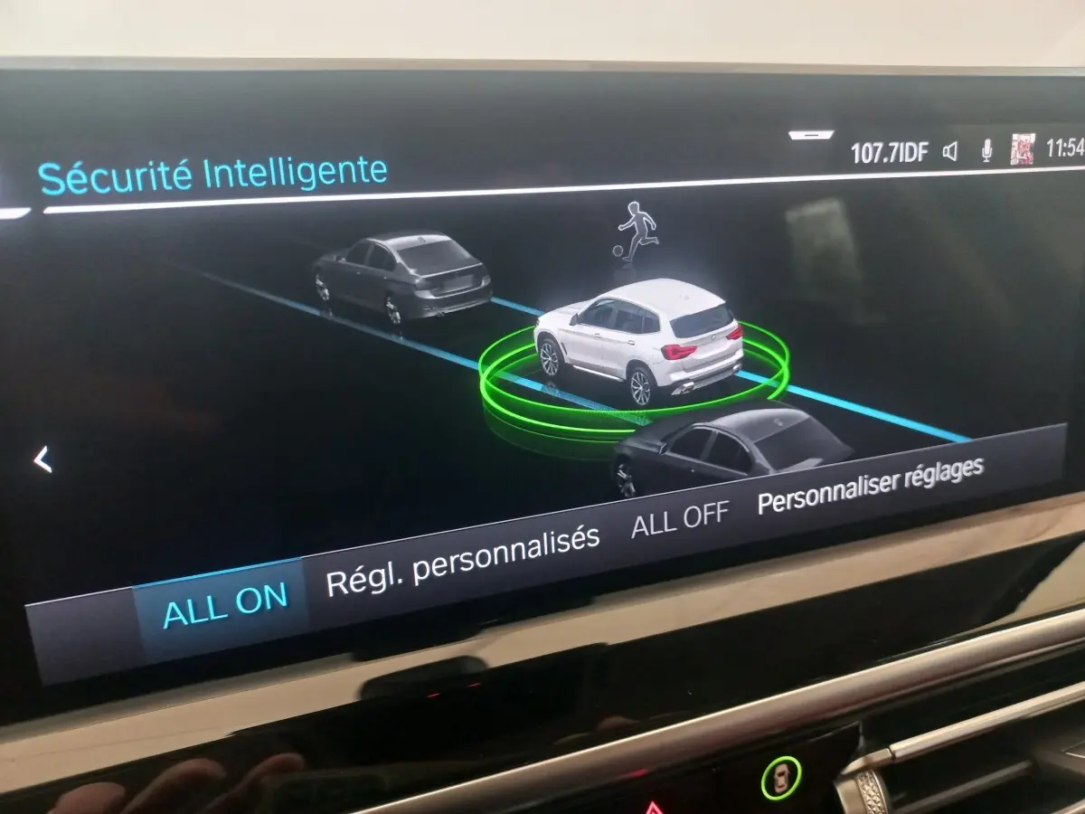 Affichage intérieur BMW X3 blanc vu de 3/4 arrière sur écran de sécurité intelligente avec véhicules gris autour.