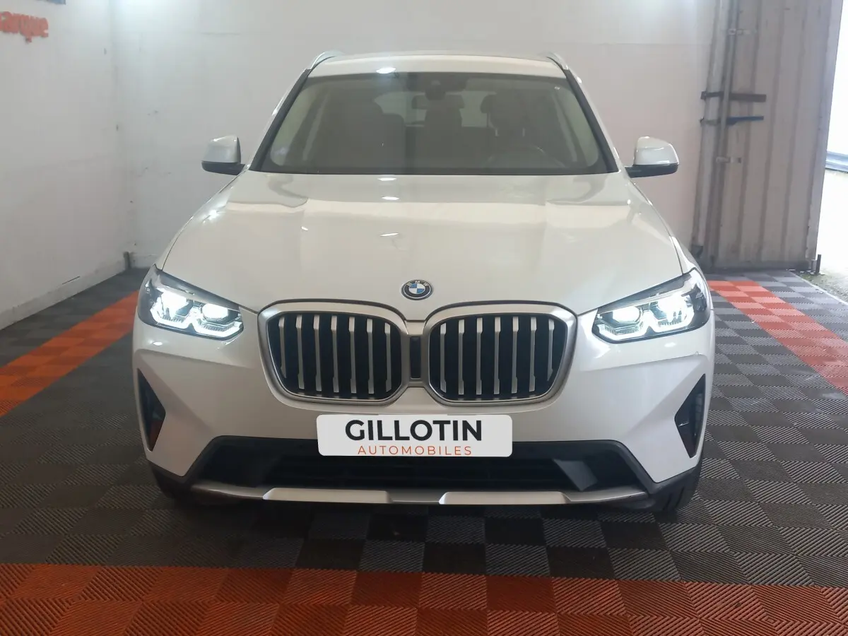 Vue frontale d’un BMW X3 blanc avec phares LED allumés et calandre double haricot caractéristique.