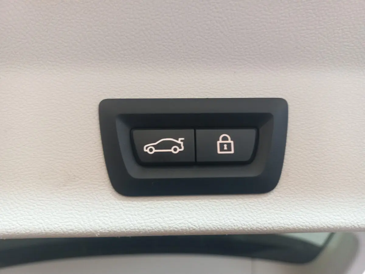 Gros plan sur les boutons d'ouverture et de verrouillage du coffre, intérieur blanc du BMW X3 hybride rechargeable.