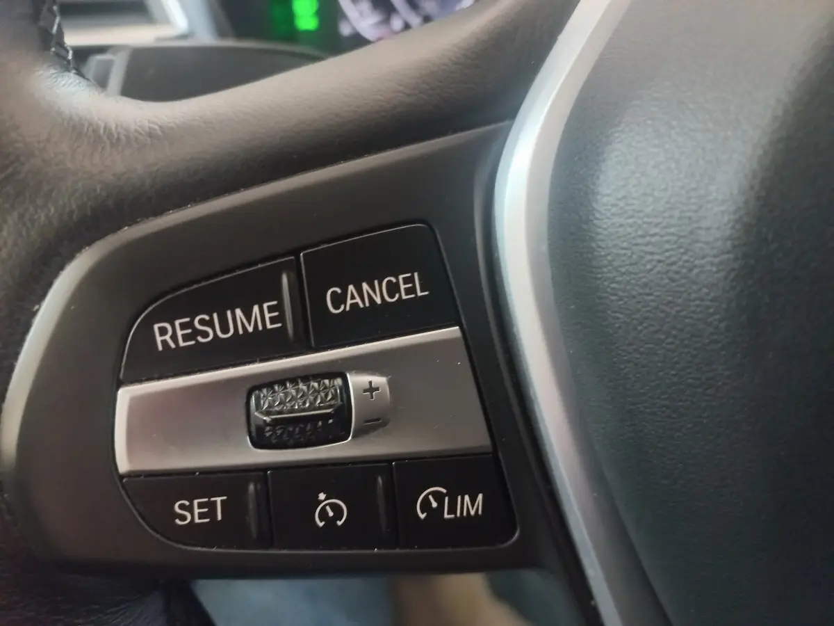 Gros plan sur les commandes du régulateur de vitesse au volant cuir d'une BMW X3 blanc hybride rechargeable.