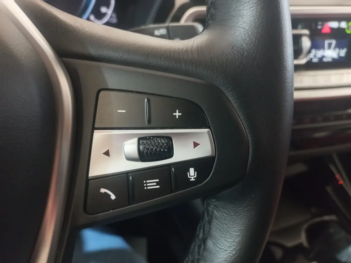 Gros plan sur les commandes multifonctions en cuir noir du volant du BMW X3 xDrive30e blanc, intérieur moderne.