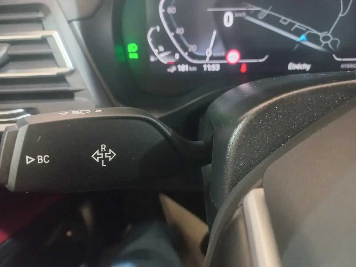 Gros plan sur la manette de clignotant gauche du tableau de bord du BMW X3 blanc, avec affichage digital en arrière-plan.