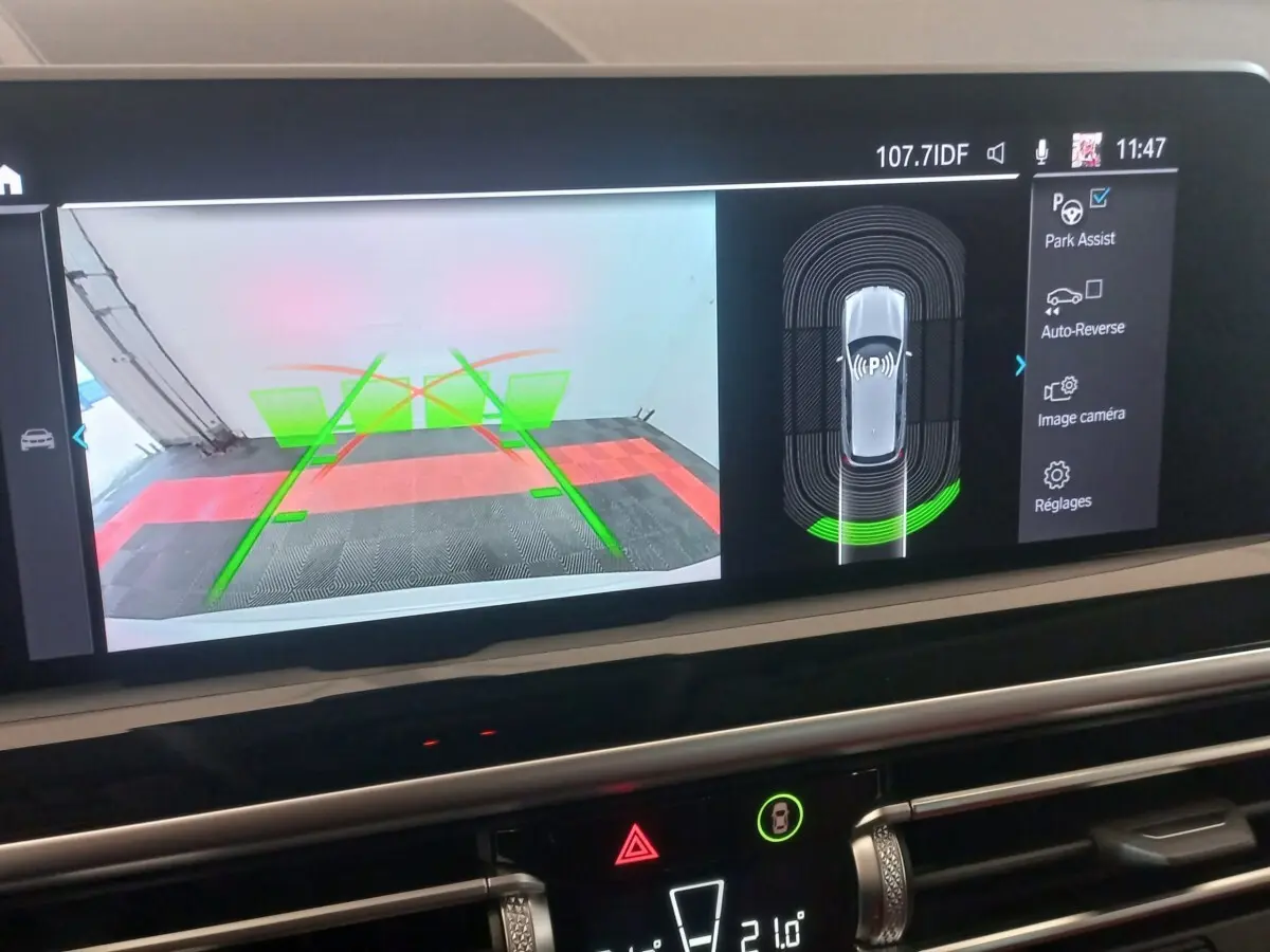 Écran tactile intérieur montrant l'aide au stationnement et la caméra de recul du BMW X3 blanc, vue de face.
