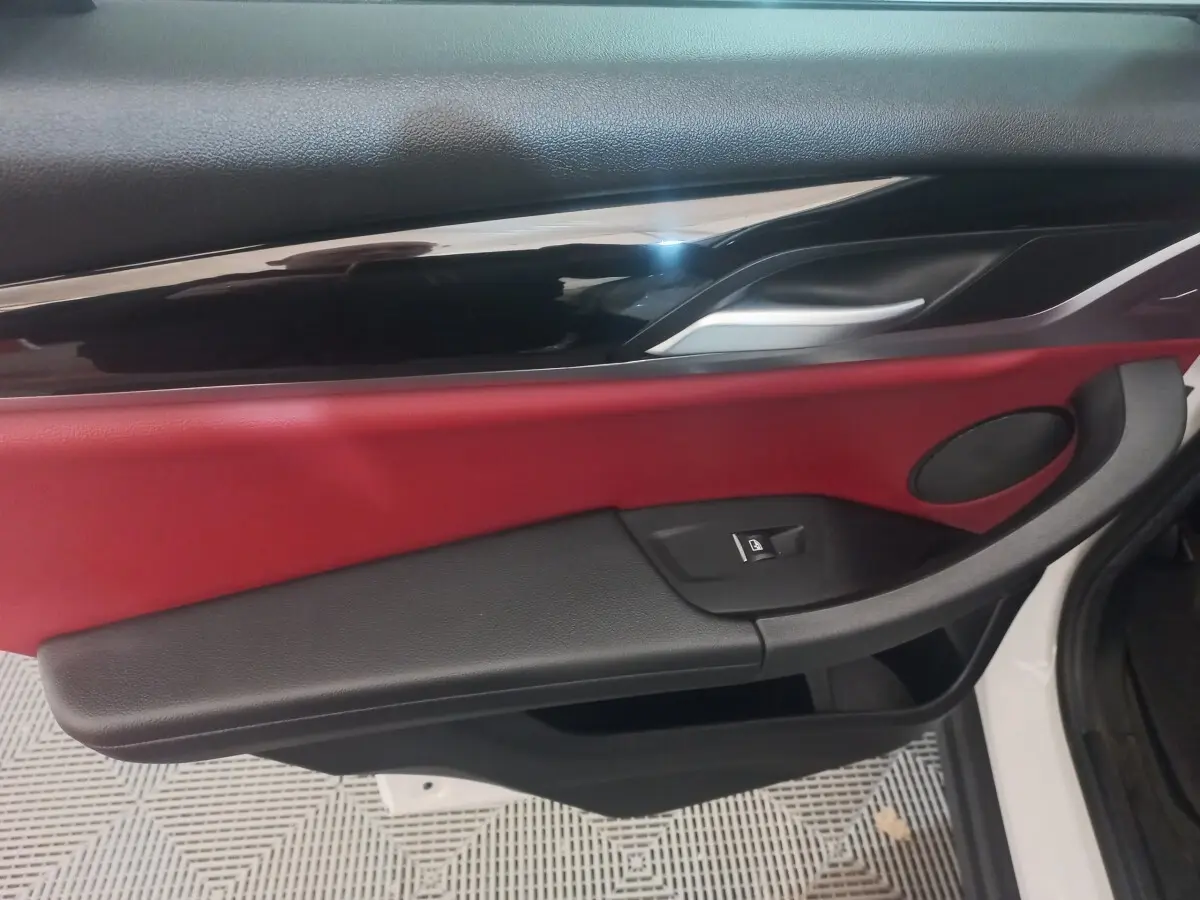Vue intérieure côté gauche de la porte avant d’un BMW X3 blanc, avec garniture rouge et noire et poignée argentée.