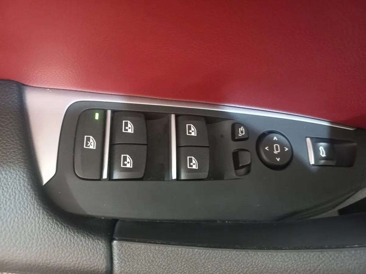 Gros plan sur les commandes des vitres et rétroviseurs côté conducteur, garniture cuir rouge et noir visible.