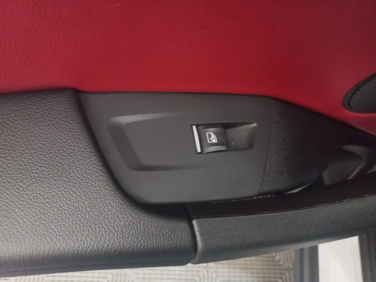 Gros plan sur le bouton de commande de lève-vitre dans l’habitacle rouge et noir d’un BMW X3 blanc.