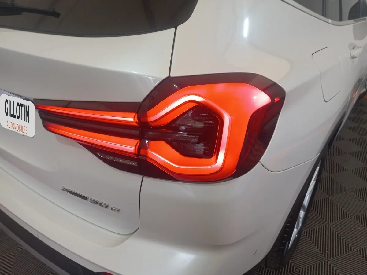 Feu arrière droit allumé d’un BMW X3 xDrive30e blanc, vue en gros plan sur l’arrière droit.