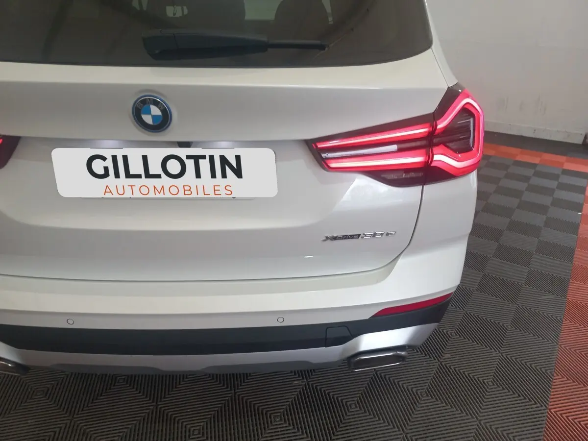 Vue arrière d’un BMW X3 xDrive30e blanc avec feux arrière LED allumés et double sortie d’échappement visible.