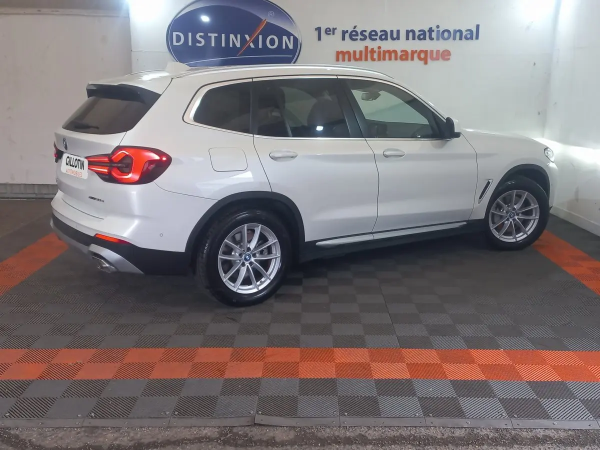 BMW X3 xDrive30e blanc en vue profil droit, avec feux arrière allumés dans un showroom intérieur.