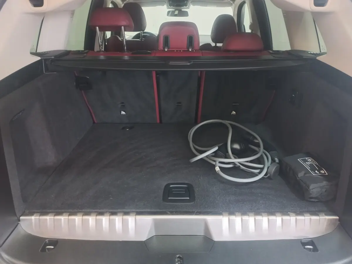 Coffre ouvert vu de l'arrière du BMW X3 blanc, avec câbles de recharge et sièges arrière rouges visibles.