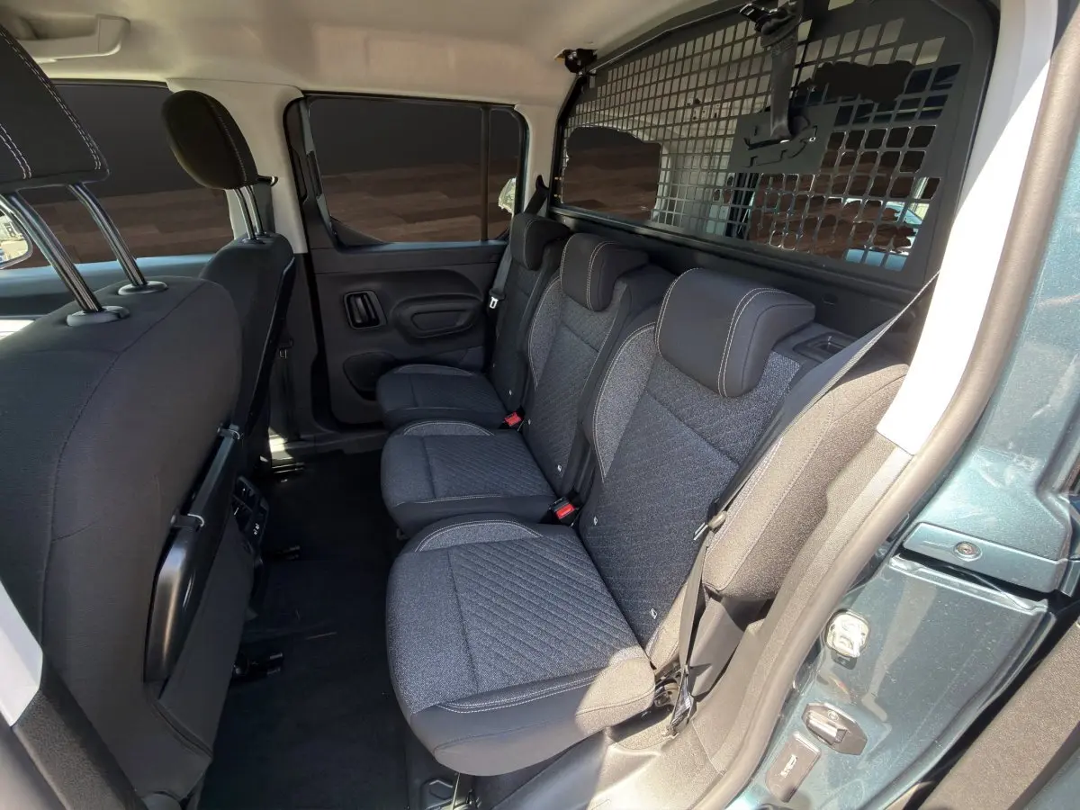 Vue intérieure côté droit des sièges arrière gris foncé du Peugeot Rifter bleu avec séparation grillagée vers le coffre.