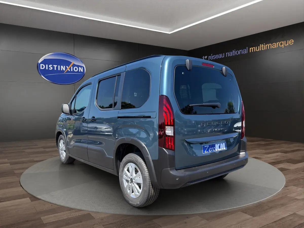 Vue 3/4 arrière droite d'un Peugeot Rifter bleu 2026 avec feux arrière LED et jantes argentées en showroom.