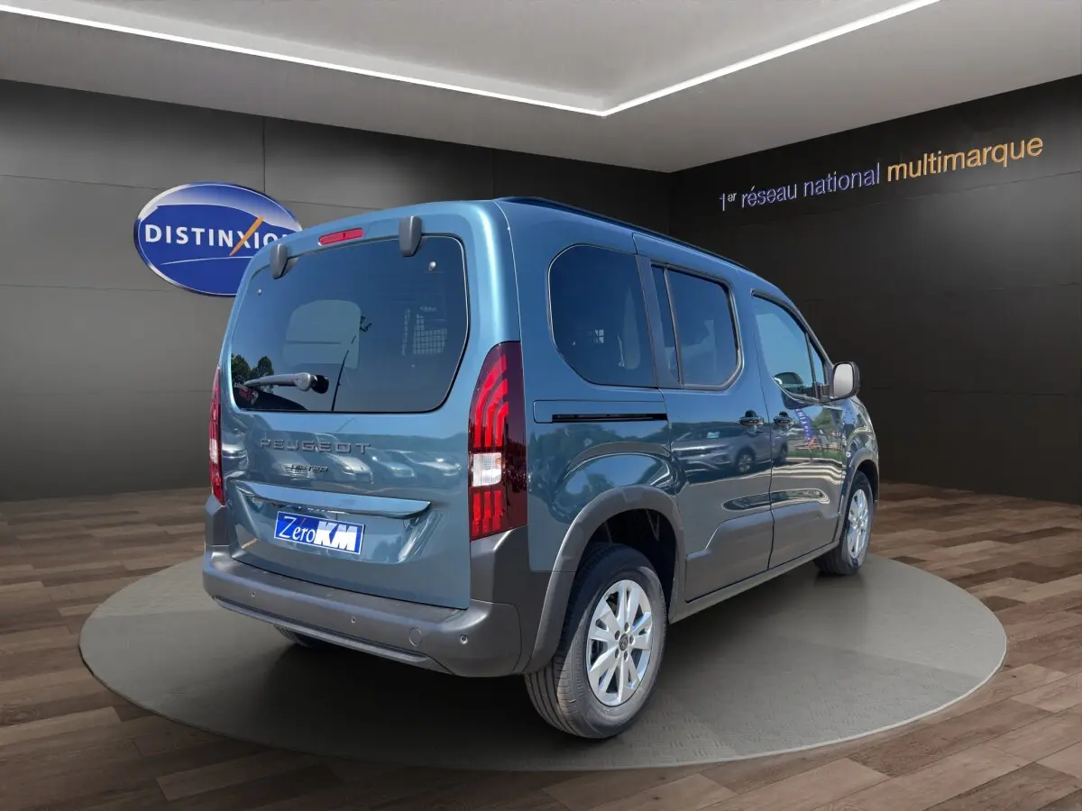 Vue 3/4 arrière droite du Peugeot Rifter bleu 2026 avec feux arrière verticaux et hayon vitré dans un showroom.