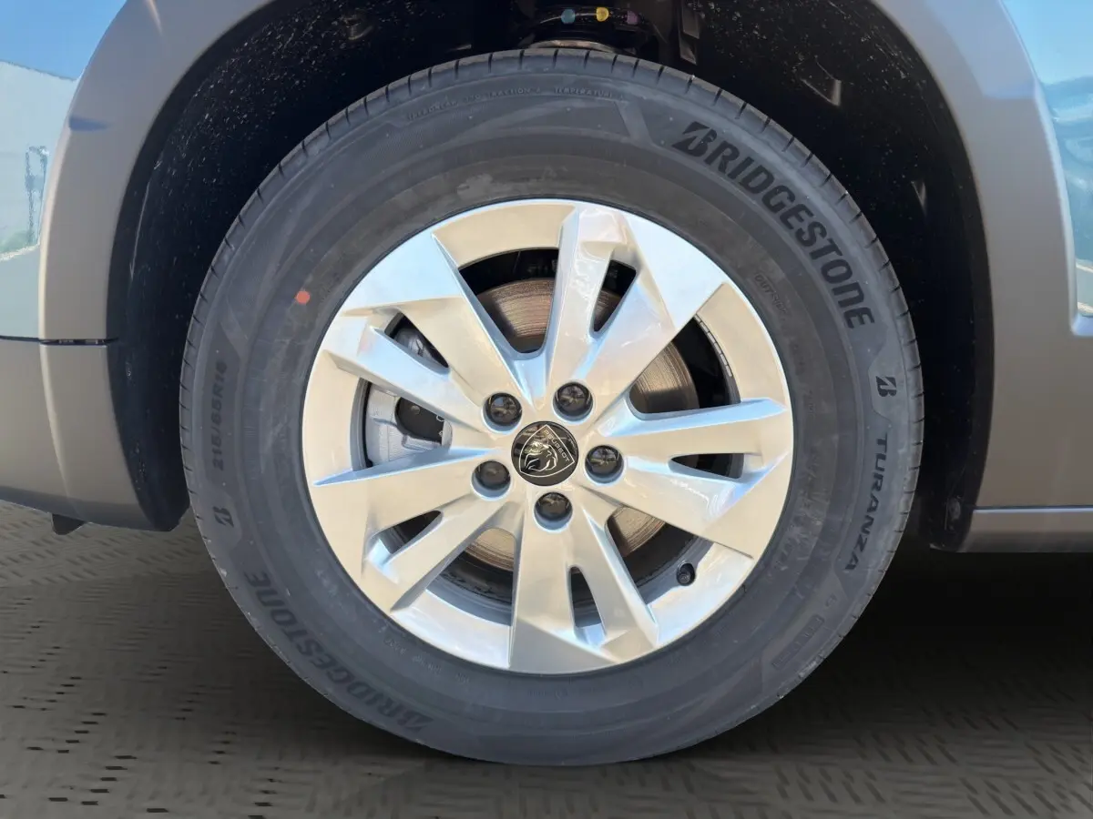 Gros plan sur la roue avant gauche d’un Peugeot Rifter bleu, jante alliage argent avec logo Peugeot central.