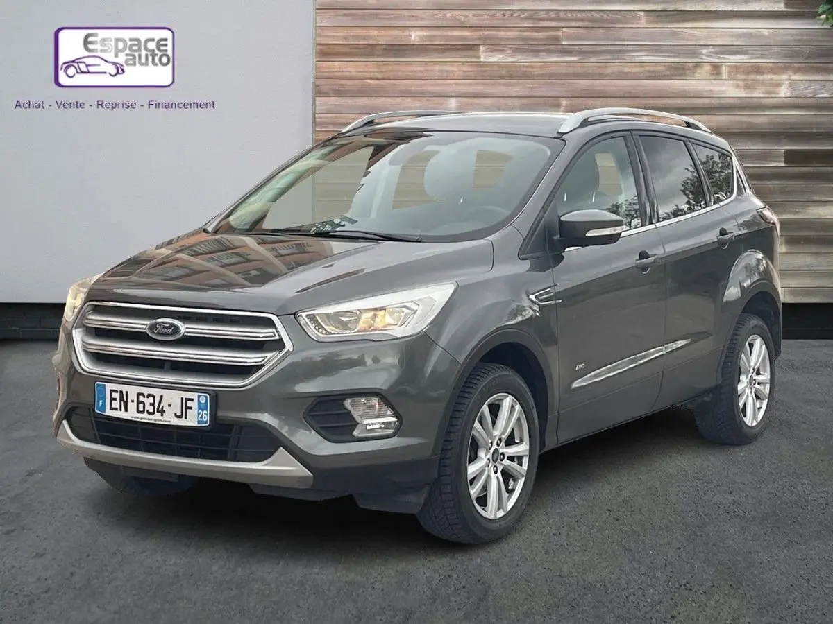 Ford Kuga gris en 3/4 avant droit, SUV compact avec calandre chromée et jantes alliage visibles.