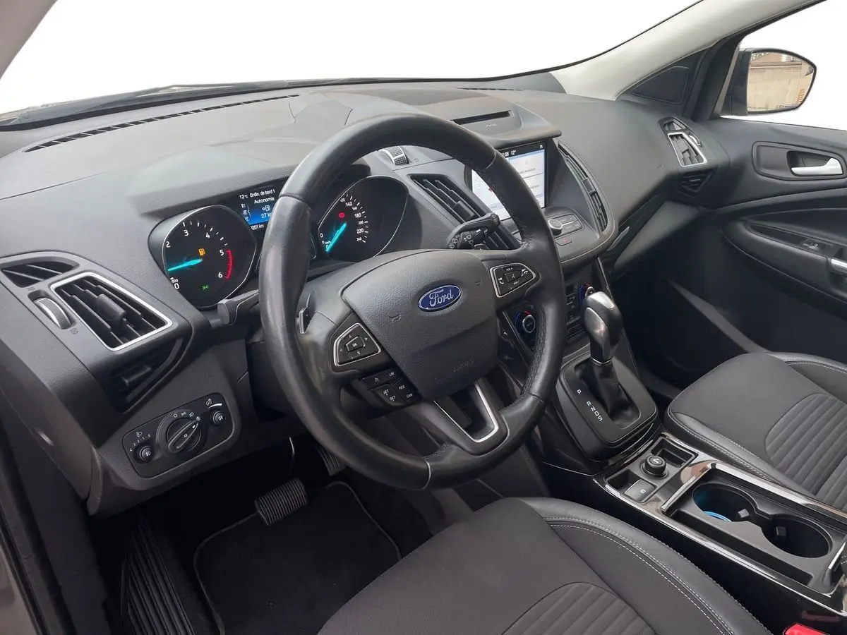 Vue intérieure côté conducteur du Ford Kuga 2017, tableau de bord noir avec volant multifonction et console centrale moderne.
