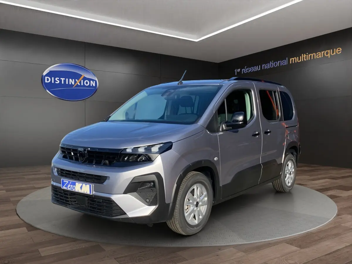 Peugeot Rifter gris clair vu en 3/4 avant droit, avec calandre noire et jantes argentées, en showroom intérieur.