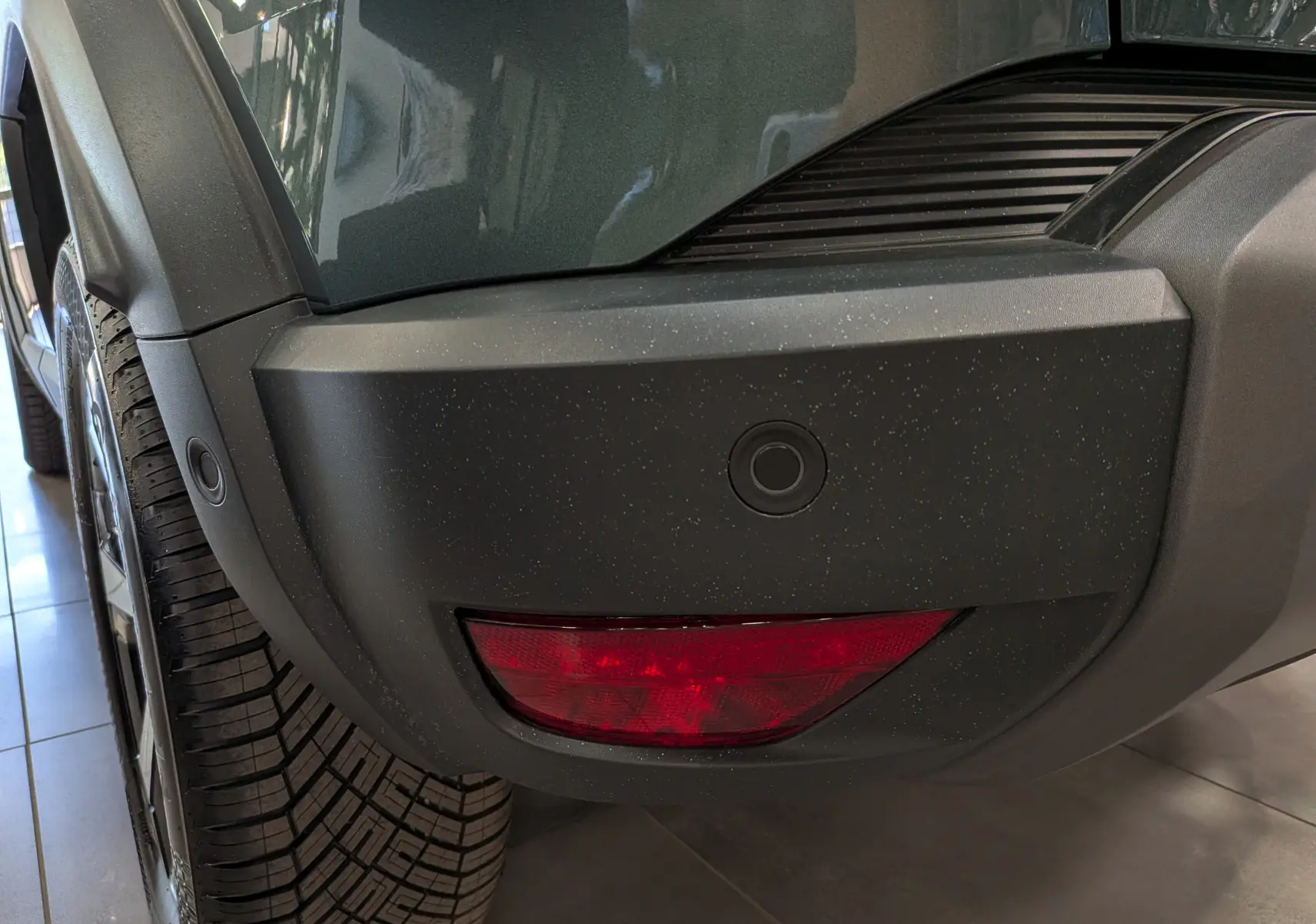 Gros plan sur l'angle arrière gauche du Dacia Duster Vert Cèdre, mettant en valeur le pare-chocs et le feu arrière rouge.