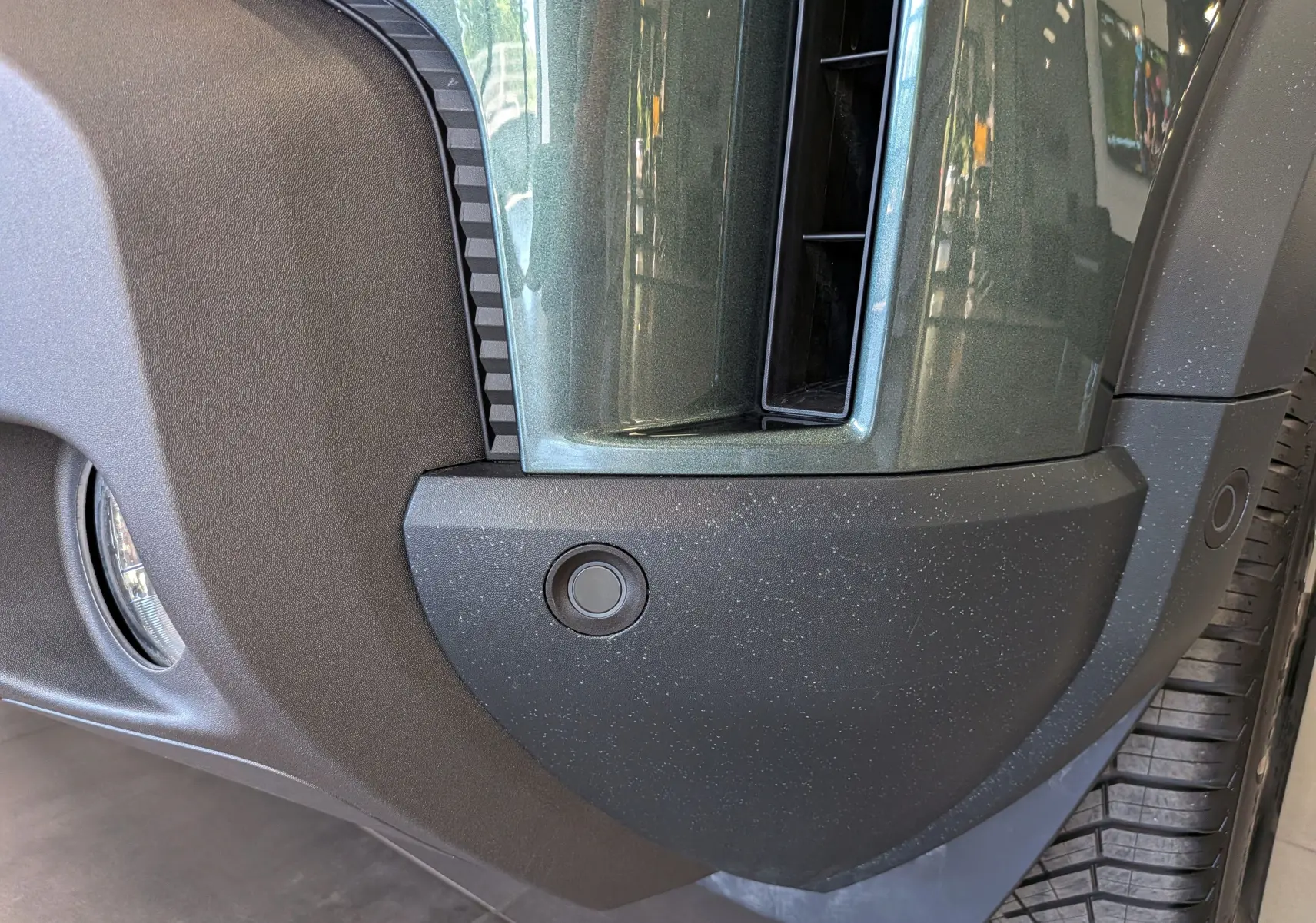 Gros plan sur le pare-chocs avant vert cèdre du Dacia Duster Hybrid-G 150 CH 4x4 avec capteur de stationnement visible.