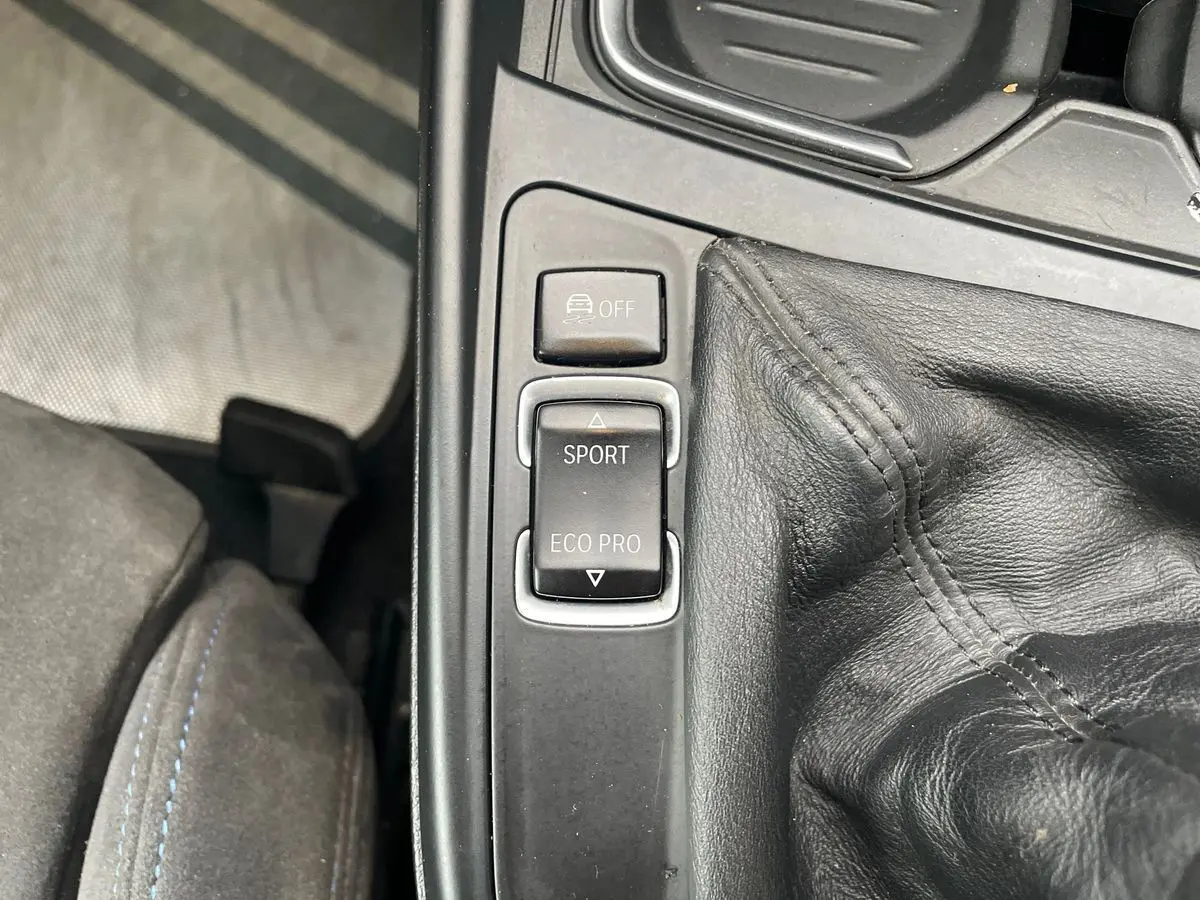 Gros plan sur la console centrale de la BMW Série 2 Coupé F22 blanche, montrant les boutons mode Sport et Eco Pro près du levier de vitesse cuir.