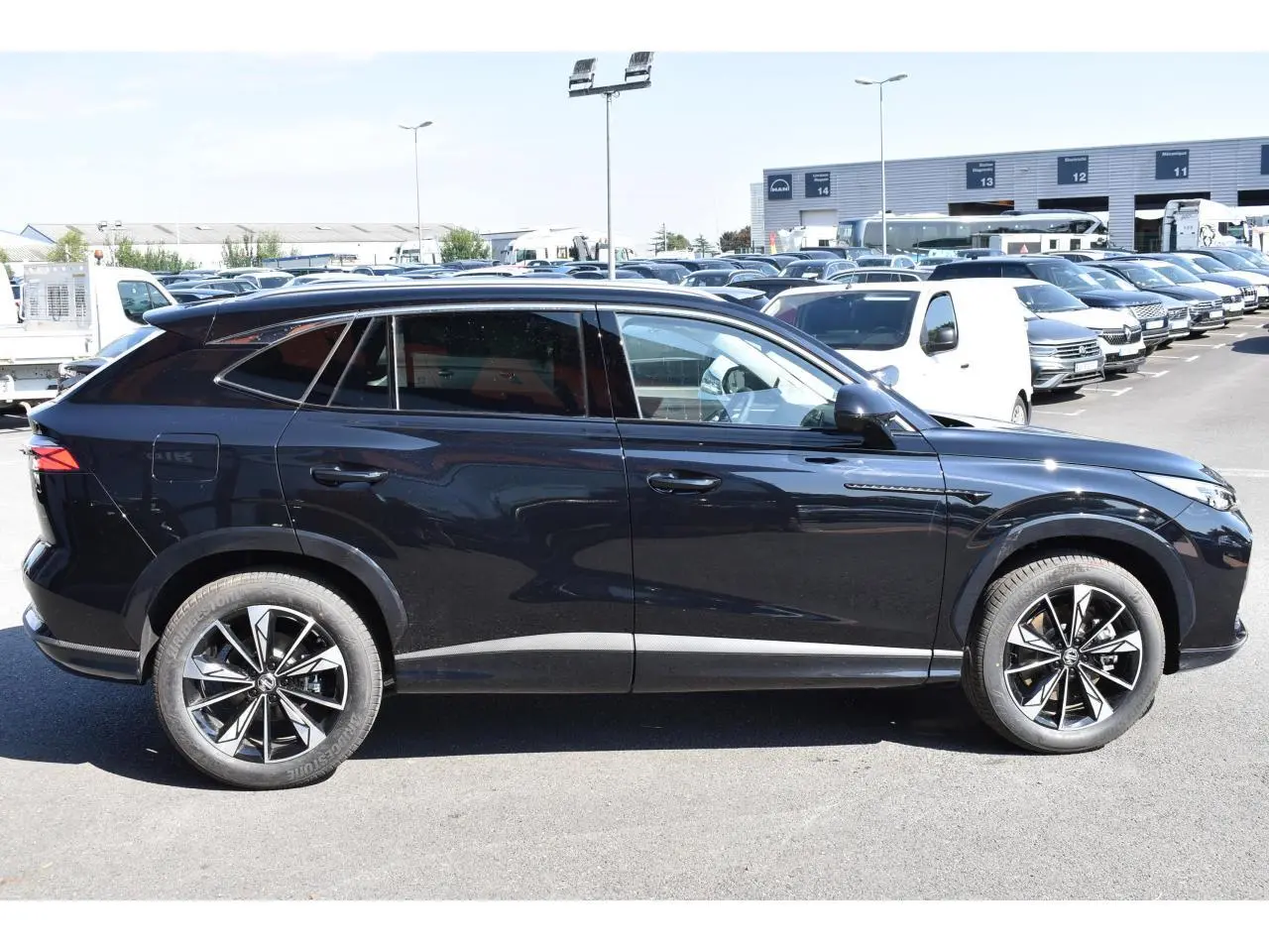 Profil côté gauche du MG Motor EHS 1.5 Hybrid+ noir métallisé avec jantes alliage 19 pouces sur parking.