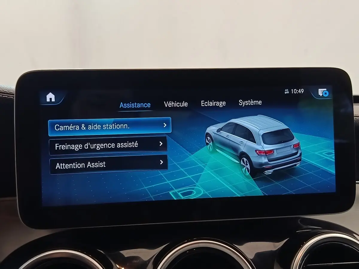 Écran tactile intérieur affichant l'assistance au stationnement avec vue 3/4 arrière d'un SUV Mercedes GLC gris.