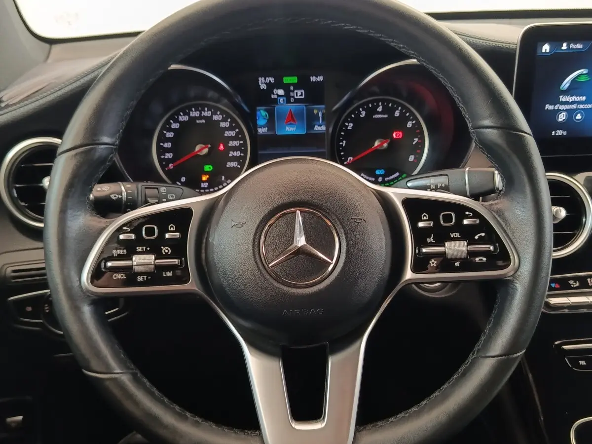 Vue rapprochée du volant cuir et aluminium d’un Mercedes GLC 300 hybride rechargeable, avec tableau de bord digital allumé.